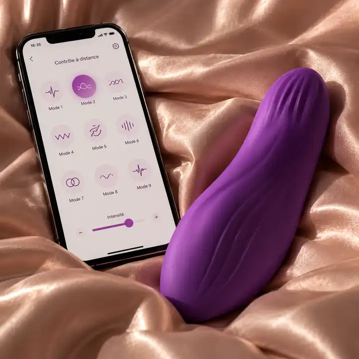 La Complice violet posé sur un drap satiné, à côté d'un smartphone affichant l'application de contrôle